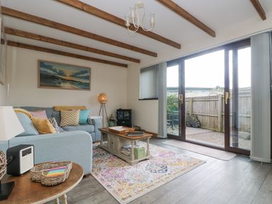 A living room with blue sofa and wooden coffee table near glass doors leading to a patio at The Lily Pad in Camborne