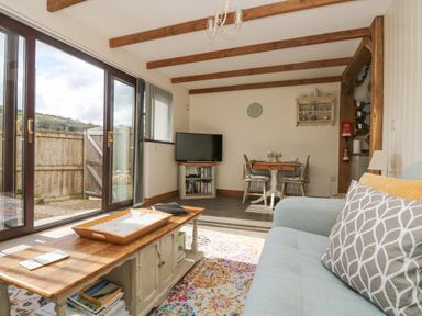 A living room with a wooden coffee table books sofa and dining table near glass sliding doors at The Lily Pad in Camborne