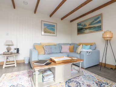 A living room with a blue sectional sofa and colorful cushions a wooden coffee table with books and a rug at The Lily Pad in Camborne