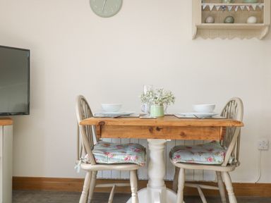 A wooden dining table with two chairs set with dishes and flowers at The Lily Pad in Camborne