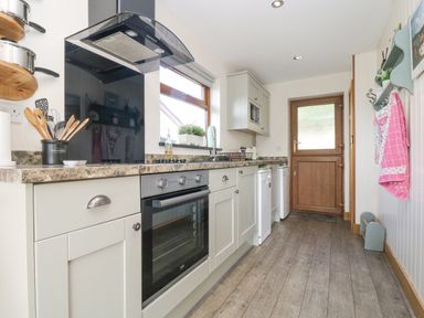 A kitchen with white cabinets an oven wooden utensils and a wooden door at The Lily Pad in Camborne