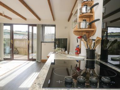 A kitchen with a cooktop a utensil holder and pots on shelves next to a dining area with a table through glass doors at The Lily Pad in Camborne