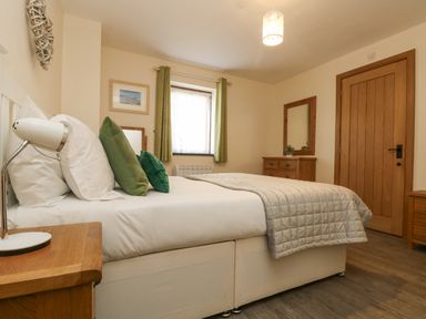 A bedroom with a bed with green pillows a wooden bedside table and a wooden dresser with a mirror at The Lily Pad in Camborne