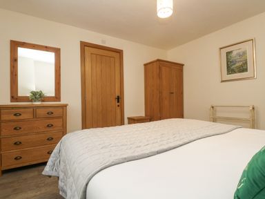 A bedroom with a bed a wooden dresser with a mirror a wooden wardrobe a wooden door and a framed picture on the wall at The Lily Pad in Camborne