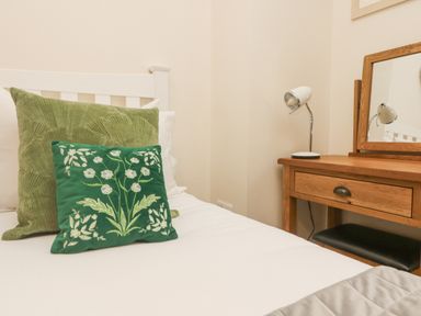 A bed with two green pillows next to a wooden dressing table with a mirror and a lamp at The Lily Pad in Camborne