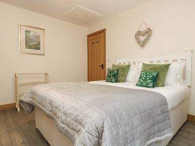 A bedroom with a double bed with green and floral pillows a grey quilt a door a wall hanging and a painting at The Lily Pad in Camborne