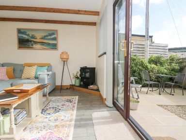 A living room with a couch pillows coffee table and a lamp next to an open glass door leading to a patio with chairs and a table at The Lily Pad in Camborne