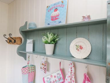 A green wooden shelf with decorative items hanging pots and hooks at The Lily Pad in Camborne