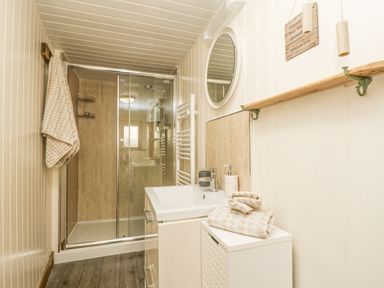 A bathroom with a glass shower enclosure a white sink a round mirror and towels at The Lily Pad in Camborne