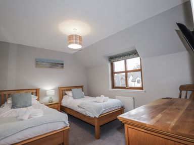 A bedroom with two single beds and a wooden table at Burnside House in Aviemore