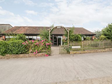 A single story building with a tiled roof and wooden fence with flowers at The Barn in Draycot Cerne near Malmesbury