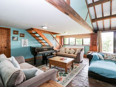 A living room with sofas a coffee table a piano and staircase at The Barn in Draycot Cerne near Malmesbury