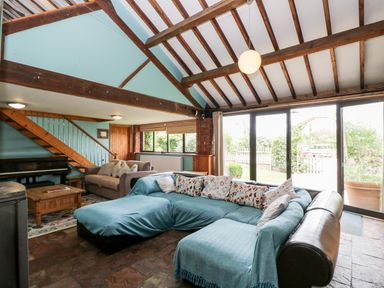 A living room with sectional sofa piano wooden coffee table and exposed beam ceiling at The Barn Draycot Cerne near Malmesbury