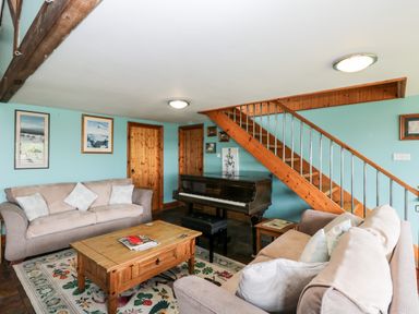 A living room with two sofas a wooden coffee table a piano and wooden stairs at The Barn in Draycot Cerne near Malmesbury