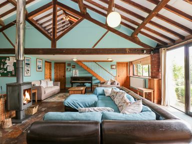 A living room with a fireplace blue sofas a piano and wooden beams at The Barn in Draycot Cerne near Malmesbury
