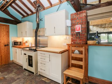 A kitchen with white cabinets a wooden chair a microwave and a stove under wooden beams at The Barn in Draycot Cerne near Malmesbury