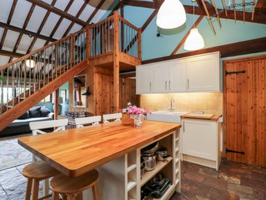 A kitchen with wooden island and stools next to staircase and sitting area at The Barn in Draycot Cerne near Malmesbury