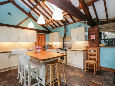 A kitchen with wooden beams white cabinets a wooden island with stools and pendant lights at The Barn Draycot Cerne near Malmesbury