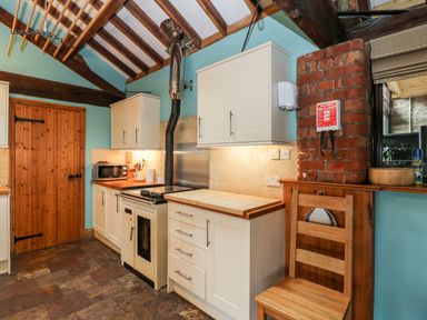 A kitchen with white cabinets a wooden door a stove a microwave and a wooden chair at The Barn in Draycot Cerne near Malmesbury