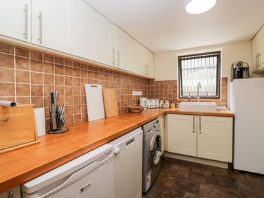 A kitchen with white cabinets wooden countertop and brown tiled backsplash at The Barn in Draycot Cerne near Malmesbury