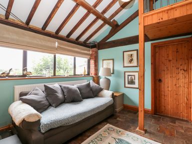 A room with a gray sofa and cushions near a window with blinds and wooden door at The Barn in Draycot Cerne near Malmesbury