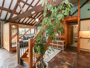 An interior space with a wooden staircase a large plant a wardrobe and a living area at The Barn in Draycot Cerne near Malmesbury