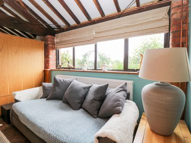 A seating area with gray cushions and a lamp on a wooden side table by a window at The Barn in Draycot Cerne near Malmesbury