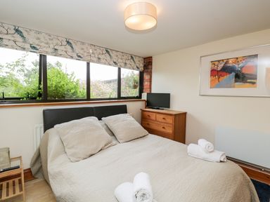A bedroom with a bed towels on it a wooden dresser with a television and a window with patterned curtains at The Barn in Draycot Cerne near Malmesbury