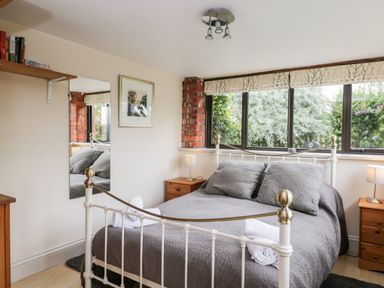 A bedroom with a metal bed frame a gray bedspread pillows bedside tables lamps a wall mirror and a window with a view of trees at The Barn in Draycot Cerne near Malmesbury