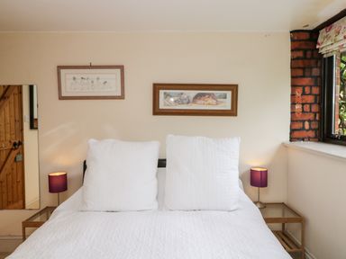 A bedroom with a bed with white bedding two purple lamps two framed pictures and a wooden door at The Barn Draycot Cerne near Malmesbury