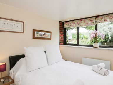 A bedroom with a bed with white bedding and pillows a window with floral curtains and a vase of flowers at The Barn in Draycot Cerne near Malmesbury