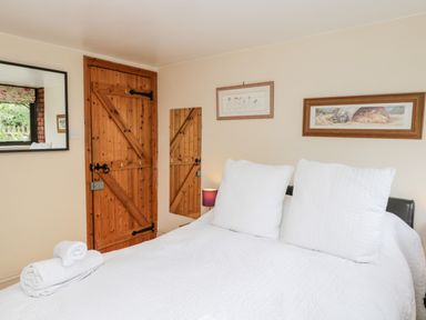 A bedroom with a wooden door a bed with white bedding and pillows and framed pictures on the wall at The Barn in Draycot Cerne near Malmesbury
