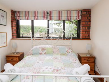 A bedroom with a white metal bed frame patchwork quilt and wooden bedside tables with lamps at The Barn in Draycot Cerne near Malmesbury