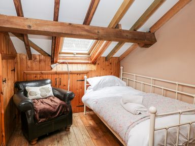 A bedroom with a single bed and black leather chair under wooden ceiling beams at The Barn in Draycot Cerne near Malmesbury