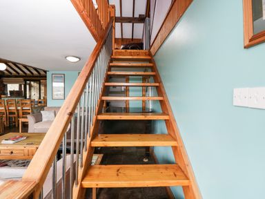 Wooden staircase with metal railings leading up from a living area with wooden dining table chairs and sofas at The Barn in Draycot Cerne near Malmesbury
