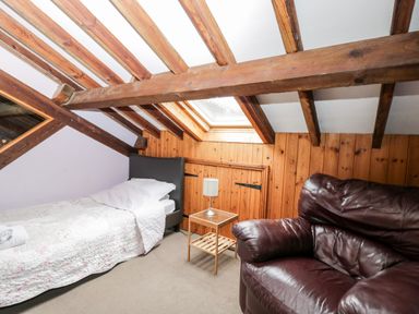 A bedroom with a single bed a bedside table and lamp and a leather armchair at The Barn in Draycot Cerne near Malmesbury