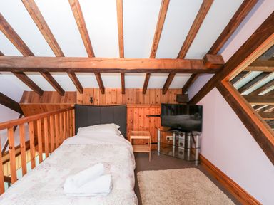 A bedroom with a single bed a small wooden table a television on a stand and wooden beams on the ceiling at The Barn in Draycot Cerne near Malmesbury