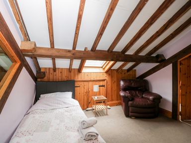 A bedroom with a single bed with white bedding a wooden side table with a lamp a brown leather armchair wooden beams on the ceiling and a skylight at The Barn Draycot Cerne near Malmesbury