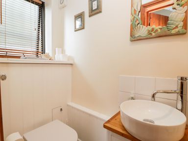 A small bathroom with a toilet a round sink on a wooden countertop a framed mirror two pictures and a window with blinds at The Barn in Draycot Cerne near Malmesbury