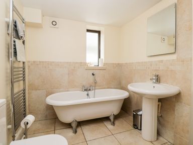 A bathroom with a bathtub sink mirror radiator and window at The Barn in Draycot Cerne near Malmesbury