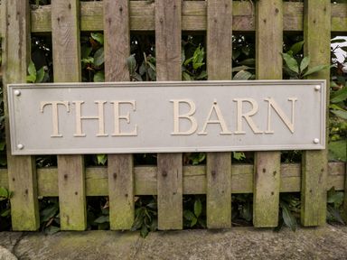 A wooden fence with a sign reading THE BARN mounted on it at The Barn in Draycot Cerne near Malmesbury