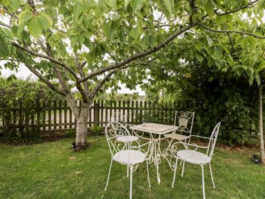 A garden area with a metal table and four chairs under a tree at The Barn in Draycot Cerne near Malmesbury