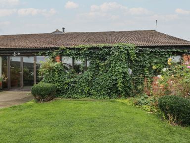 A garden with green grass in front of a brick house with ivy growing on the wall at The Barn in Draycot Cerne near Malmesbury