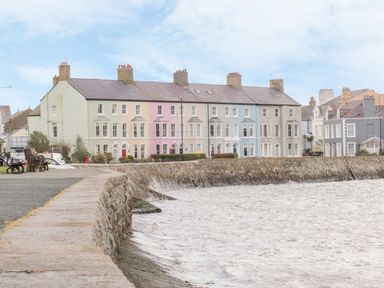 A row of pastel-colored houses along a stone seawall next to a body of water at Seion Chapel in Beaumaris