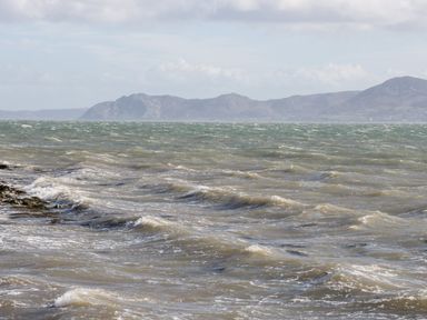 A view of a choppy sea with waves and distant mountains under a cloudy sky at Seion Chapel in Beaumaris