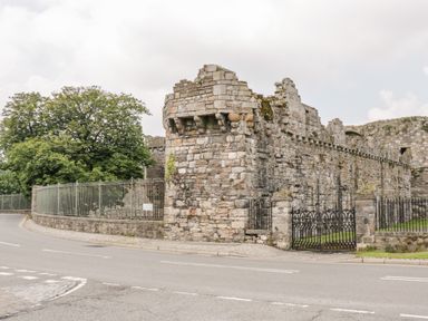 A stone castle ruin with a wrought iron gate and a road in front at Seion Chapel in Beaumaris