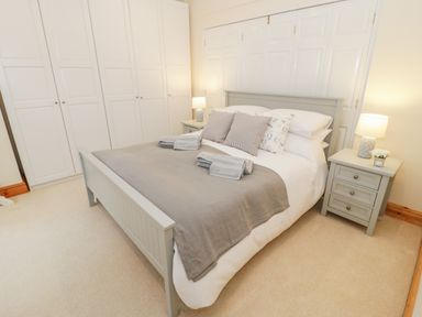 A bedroom with a double bed two bedside tables with lamps and wardrobes along one wall at Seion Chapel Beaumaris