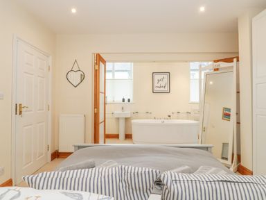A bedroom with a bed facing an open doorway leading to a bathroom with a freestanding bathtub and a pedestal sink at Seion Chapel in Beaumaris