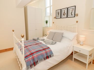 A bedroom with a white bed with striped pillows and a plaid blanket a white wardrobe a bedside table with a lamp and three framed pictures above the bed at Seion Chapel in Beaumaris