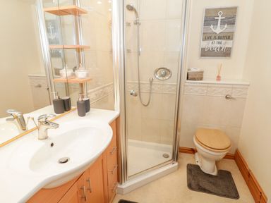 A bathroom with a sink and countertop cabinet a glass shower enclosure and a toilet with a wooden seat at Seion Chapel in Beaumaris